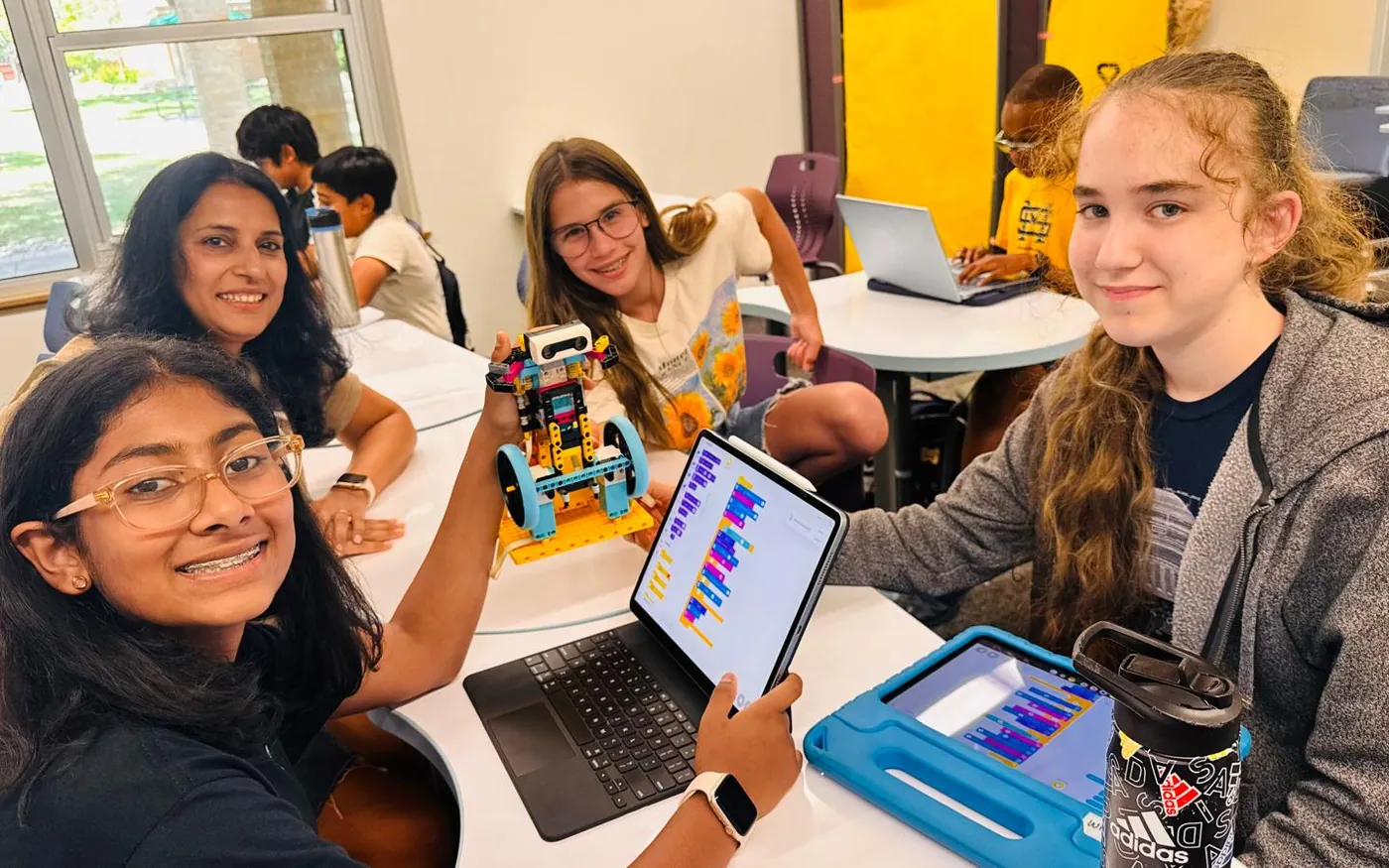 Middle school students smiling as they code a LEGO robot on tablets during a Wize robotics class